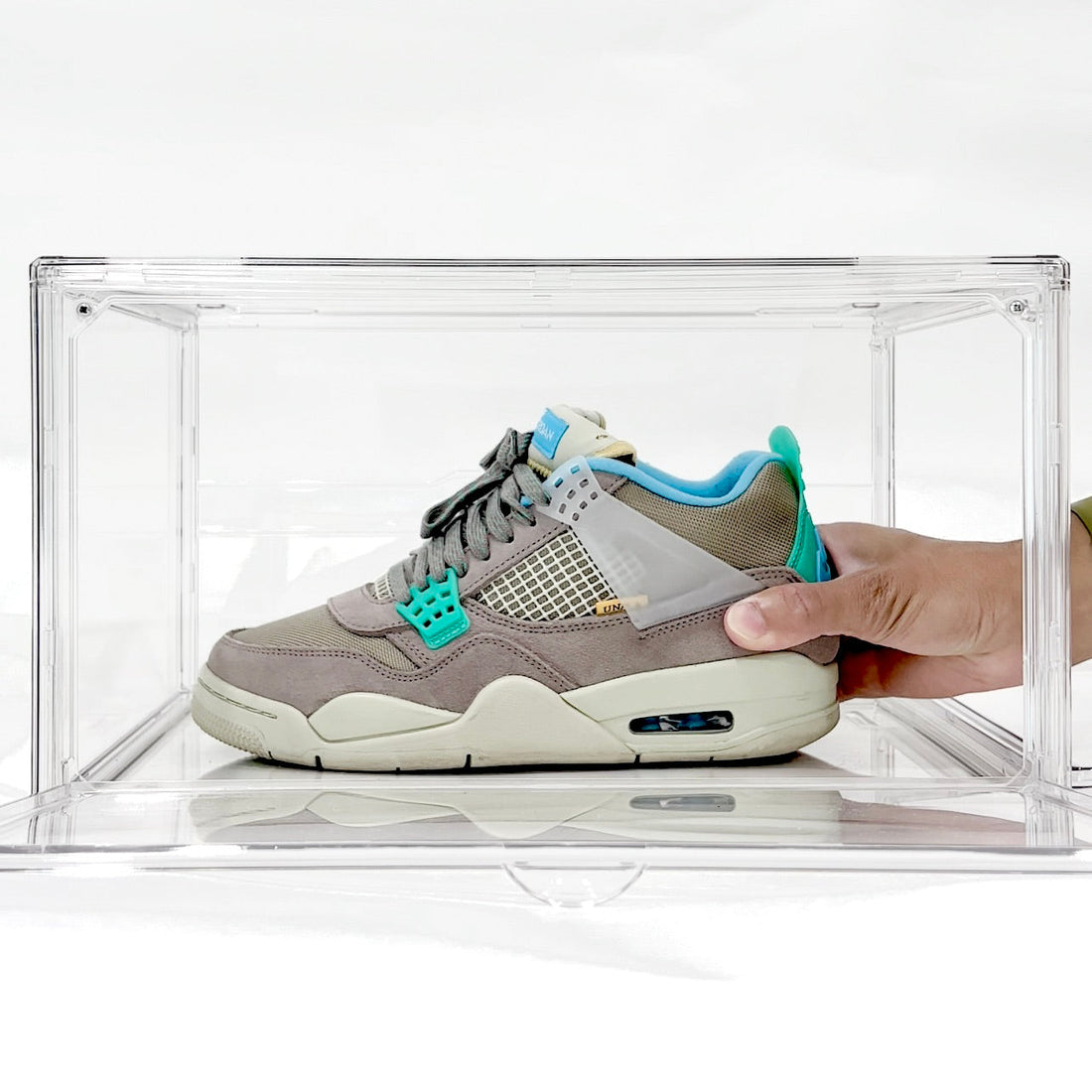 Hand placing a Jordan 4 sneaker into a clear shoe storage box
