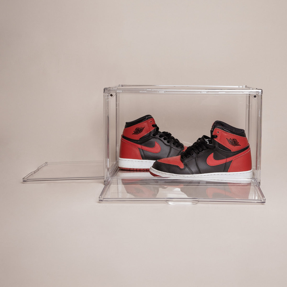 Clear stackable shoe storage box with front and side magnetic doors open, holding red and black Jordan 1 sneakers