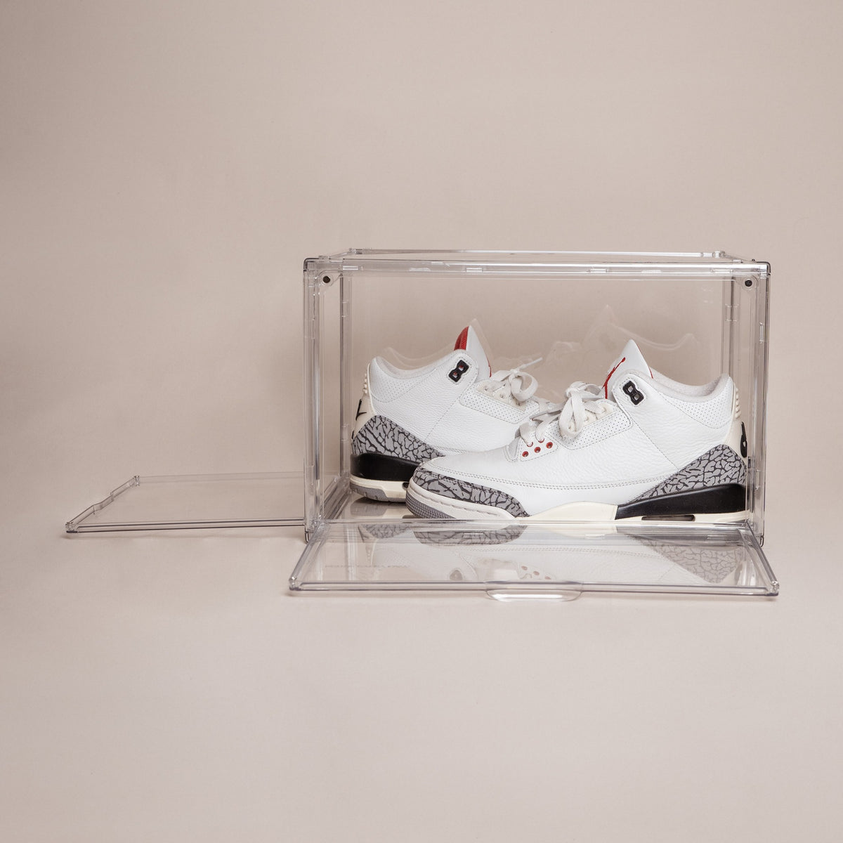 Clear stackable shoe storage box with front and side magnetic doors open, holding white and gray Jordan 3 sneakers