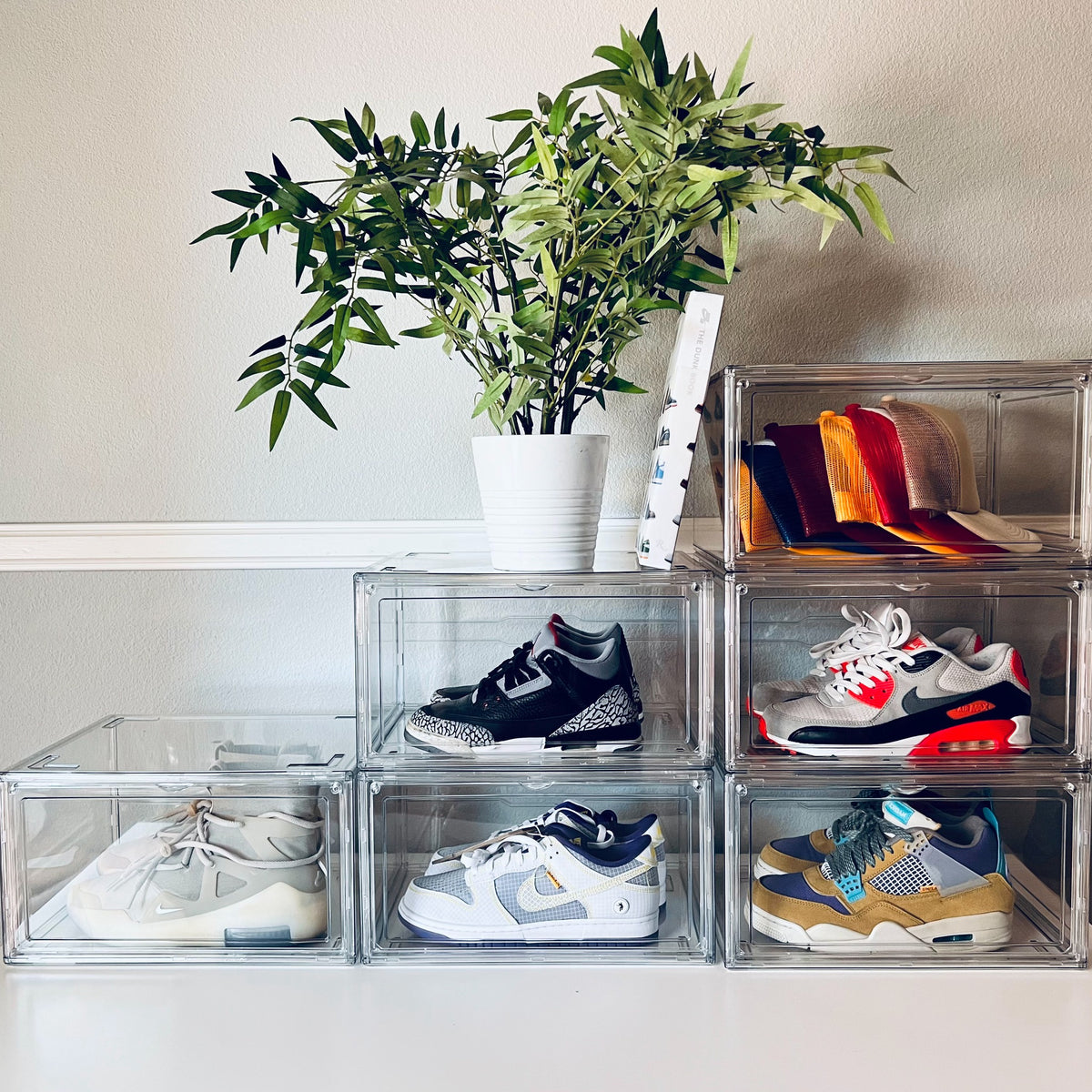 Six clear stackable shoe storage boxes on a dresser holding sneakers and hats