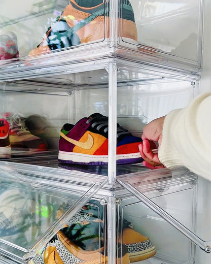 Hand pulling a sneaker out of the side door of a clear shoe box in the middle of a stack