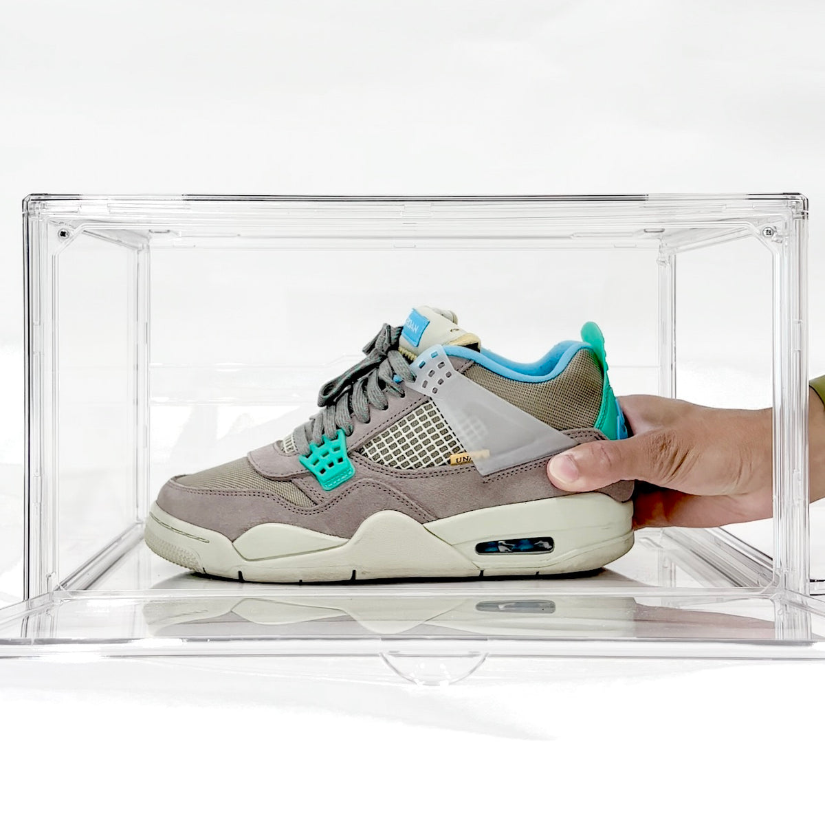 Hand placing a men's size 8 Jordan 4 sneaker into a clear shoe storage box