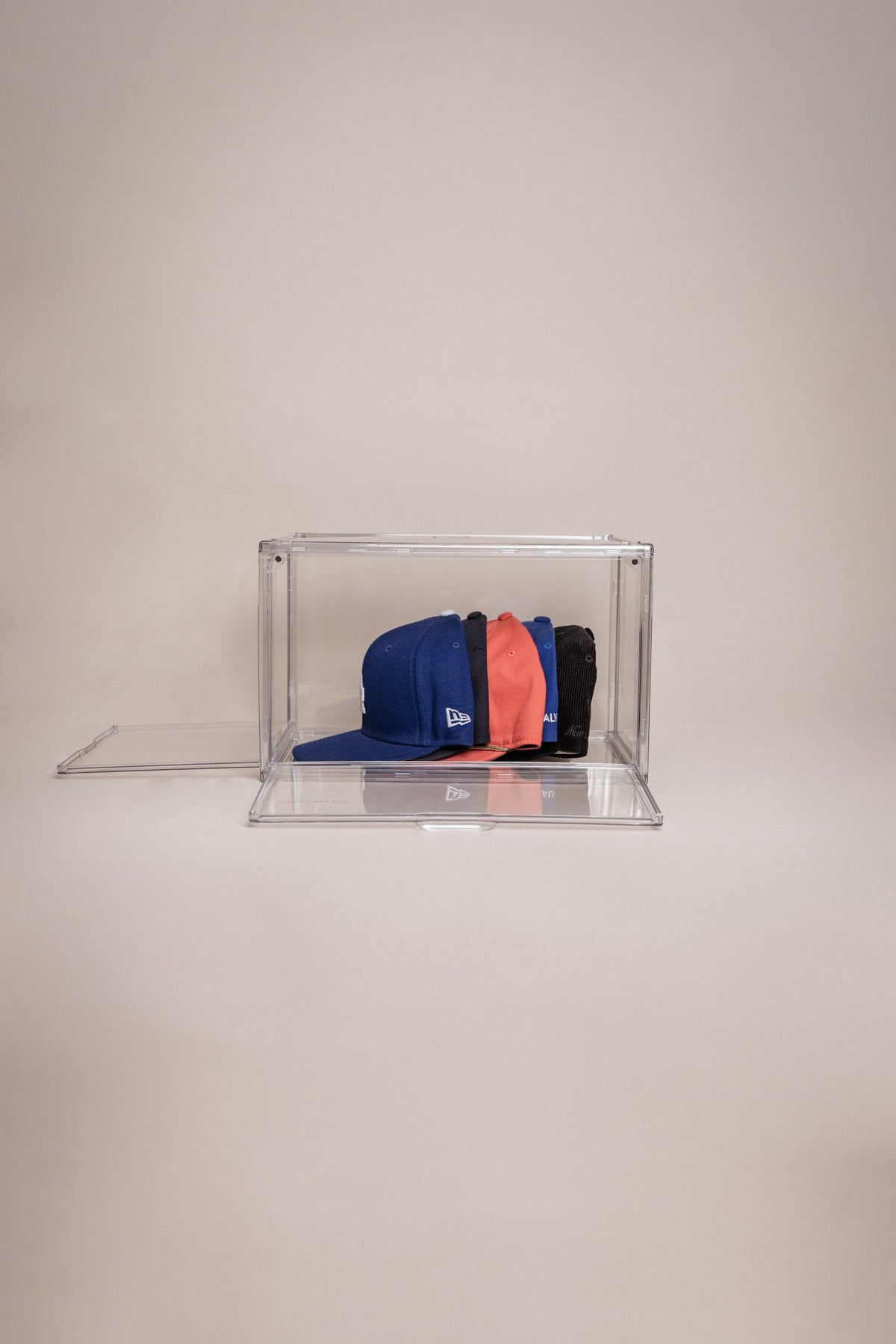 Clear shoe storage box holding a row of baseball caps